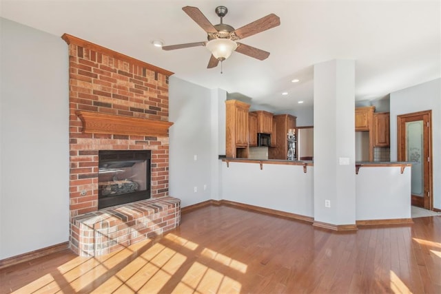 unfurnished living room featuring light wood-style floors, recessed lighting, a brick fireplace, and baseboards