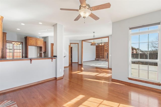 unfurnished living room with a ceiling fan, a sink, baseboards, and wood finished floors