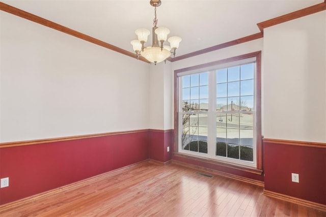 unfurnished room with ornamental molding, wood finished floors, visible vents, and a notable chandelier