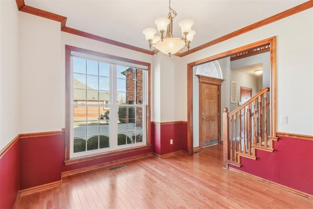 unfurnished dining area featuring visible vents, an inviting chandelier, ornamental molding, wood finished floors, and stairs