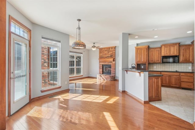 kitchen with black microwave, open floor plan, hanging light fixtures, brown cabinets, and dark countertops