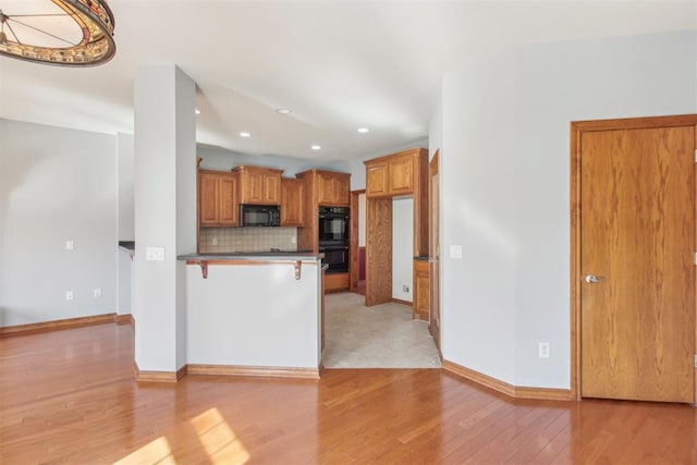 kitchen featuring backsplash, black appliances, brown cabinetry, dark countertops, and a kitchen bar