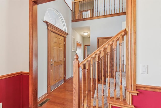 foyer entrance with visible vents, stairway, a high ceiling, wood finished floors, and baseboards