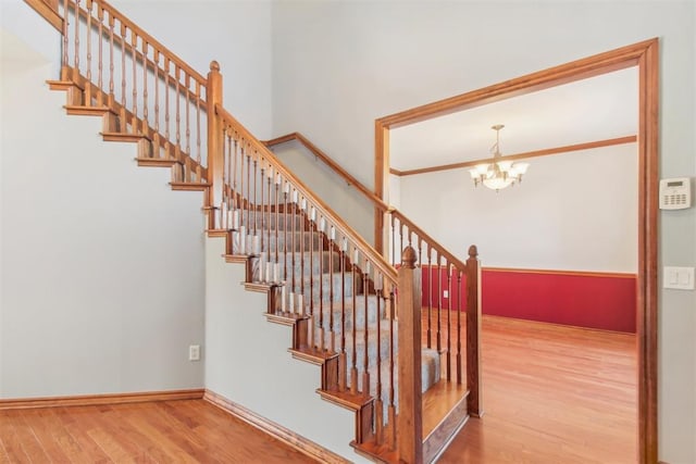 stairs featuring a chandelier, crown molding, baseboards, and wood finished floors