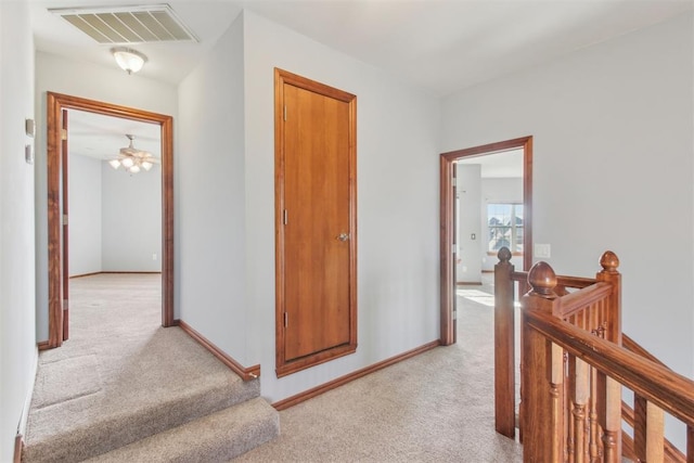 hall featuring light carpet, an upstairs landing, visible vents, and baseboards