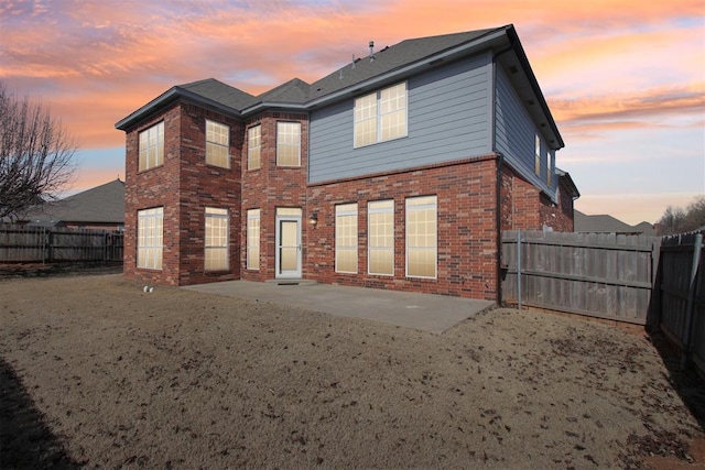 back of house at dusk with a patio area, brick siding, and a fenced backyard