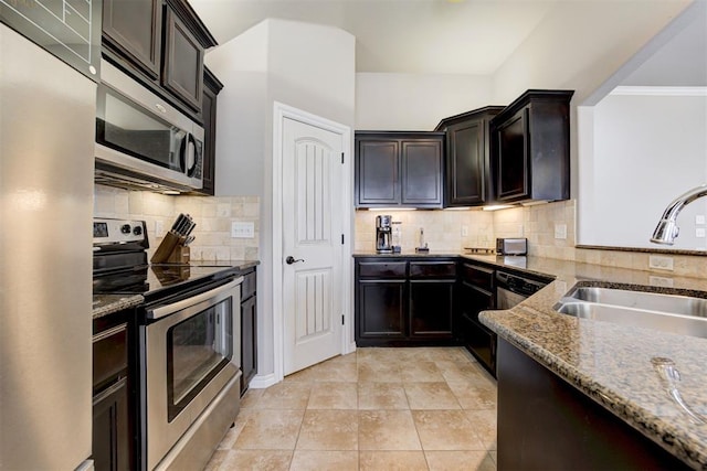 kitchen with light tile patterned floors, decorative backsplash, appliances with stainless steel finishes, a sink, and light stone countertops