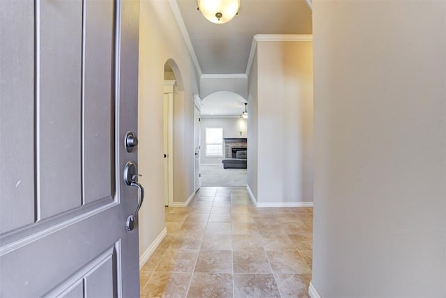 foyer with baseboards, a fireplace, arched walkways, and crown molding