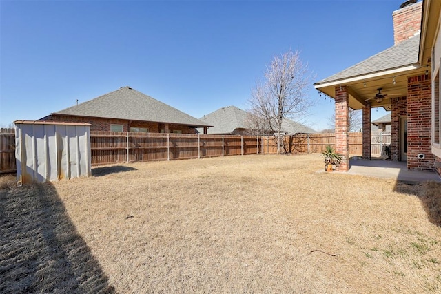 view of yard with a patio, a fenced backyard, ceiling fan, an outbuilding, and a shed