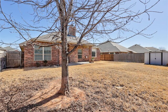 back of house featuring a fenced backyard, a chimney, a storage unit, and brick siding