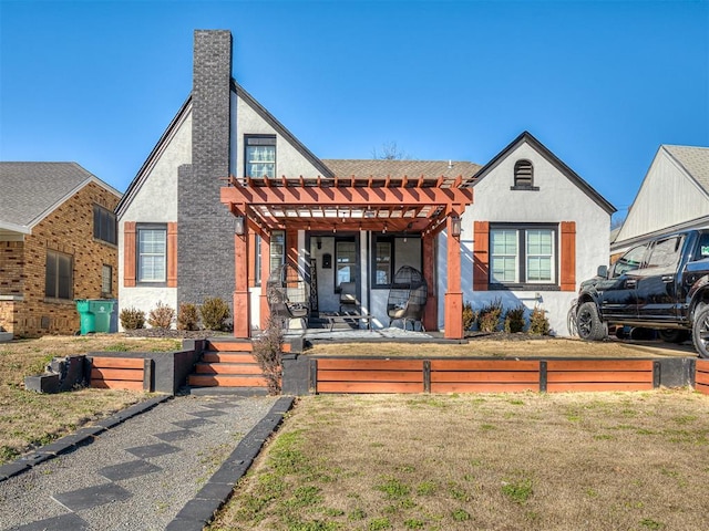 view of front of house with stucco siding, a pergola, and a front yard