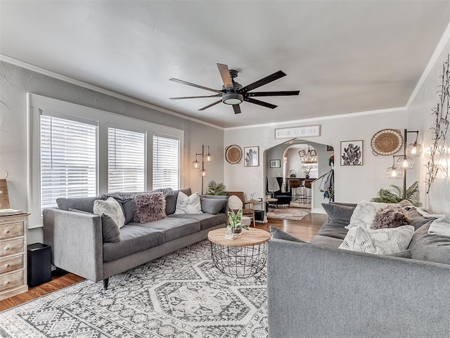 living room featuring ornamental molding, a ceiling fan, arched walkways, and light wood-type flooring