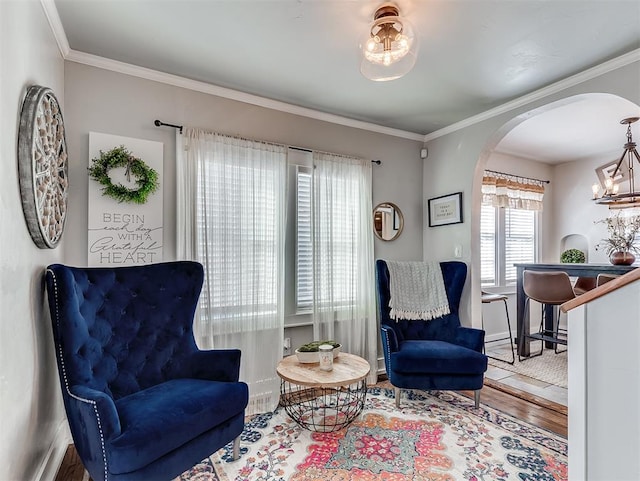 sitting room with crown molding, baseboards, a chandelier, wood finished floors, and arched walkways