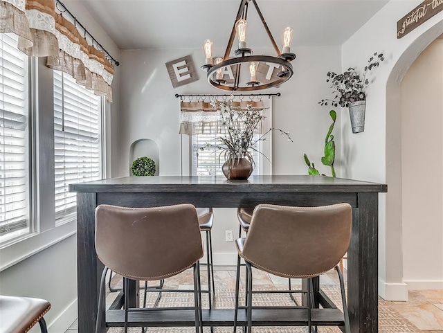 bar featuring baseboards, arched walkways, and a chandelier