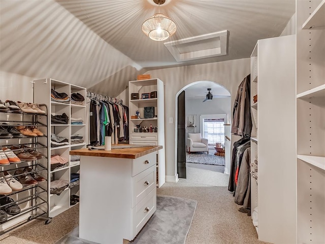 spacious closet featuring arched walkways, light carpet, and vaulted ceiling