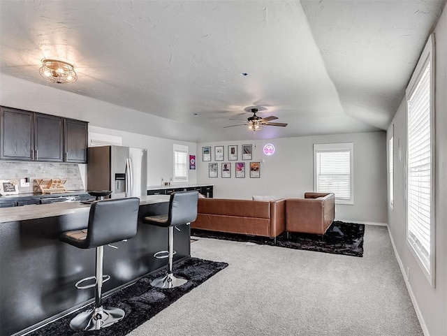 kitchen with dark brown cabinets, baseboards, light carpet, a kitchen breakfast bar, and stainless steel fridge