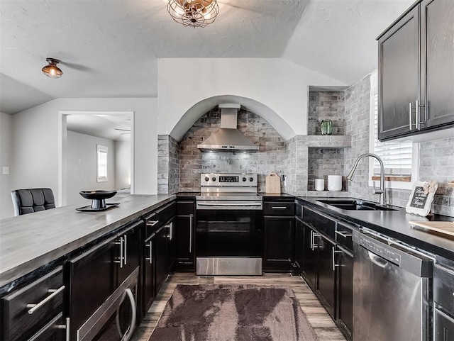 kitchen featuring a sink, dark countertops, stainless steel appliances, wall chimney range hood, and vaulted ceiling