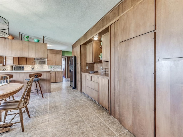 1802 N 15th St, Perry, OK 73077 - kitchen with decorative backsplash, ventilation hood, a breakfast bar area, a peninsula, and light countertops
