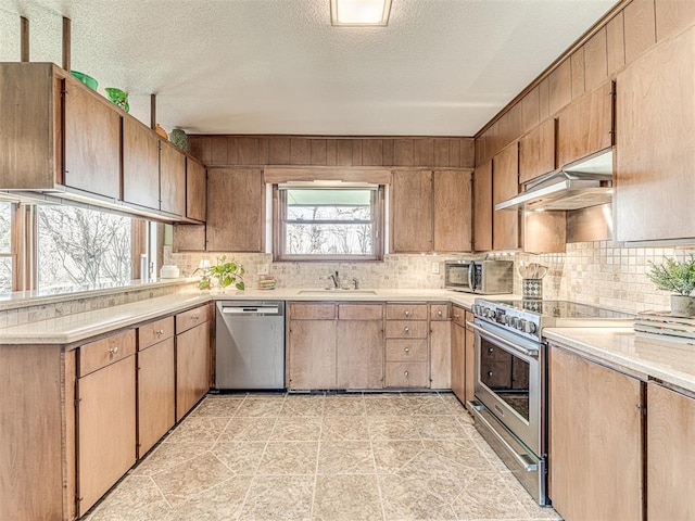 1802 N 15th St, Perry, OK 73077 - kitchen featuring appliances with stainless steel finishes, under cabinet range hood, decorative backsplash, light countertops, and a textured ceiling