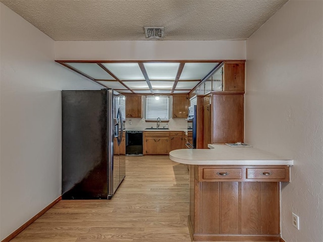 kitchen with a peninsula, a sink, light countertops, stainless steel fridge with ice dispenser, and dishwasher