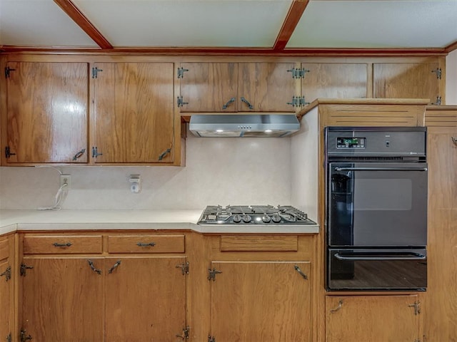 kitchen featuring a warming drawer, light countertops, stainless steel gas stovetop, and under cabinet range hood