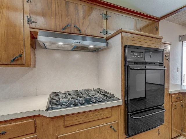 kitchen with under cabinet range hood, light countertops, a warming drawer, black appliances, and brown cabinetry