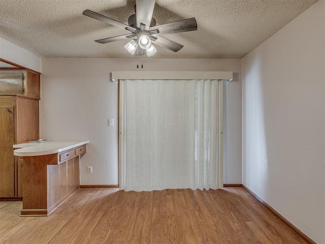 interior space featuring a ceiling fan, light wood-style flooring, brown cabinets, light countertops, and a textured ceiling