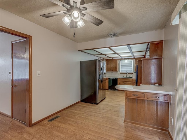 kitchen featuring light countertops, visible vents, brown cabinetry, a sink, and black appliances