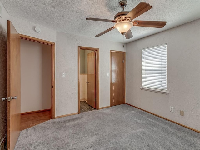 unfurnished bedroom with a textured ceiling, a textured wall, light carpet, and baseboards