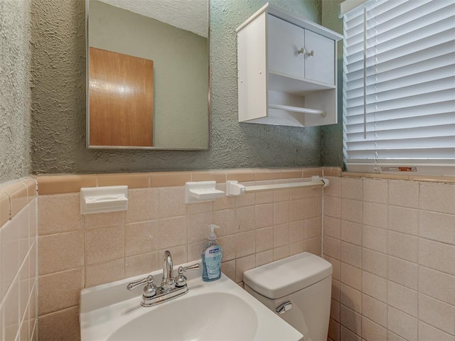 bathroom with a wainscoted wall, a textured wall, a sink, and toilet