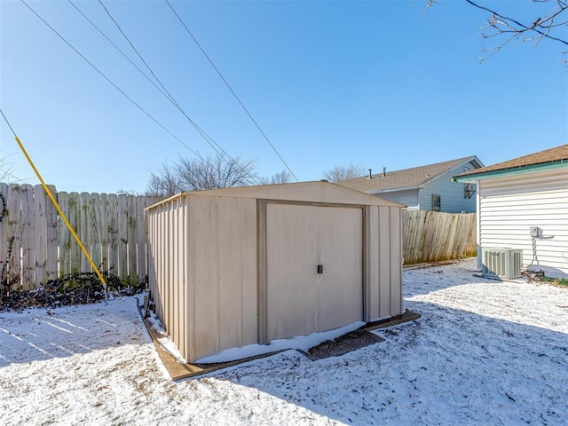 snow covered structure with central air condition unit, a storage shed, a fenced backyard, and an outdoor structure