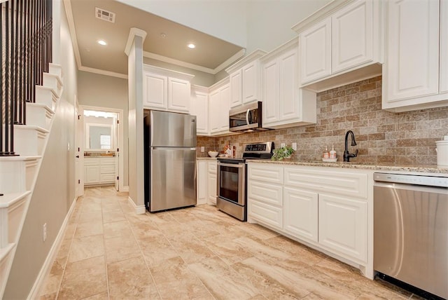 kitchen with light stone counters, stainless steel appliances, a sink, white cabinetry, and backsplash