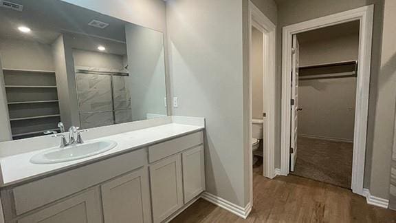 bathroom featuring toilet, hardwood / wood-style flooring, a shower with shower door, and vanity