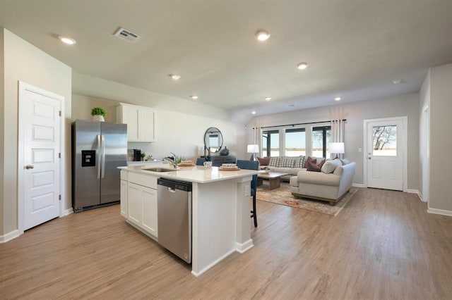 kitchen featuring appliances with stainless steel finishes, light wood-type flooring, an island with sink, sink, and white cabinetry