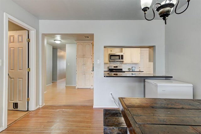 kitchen with visible vents, backsplash, stainless steel appliances, light wood-type flooring, and a notable chandelier