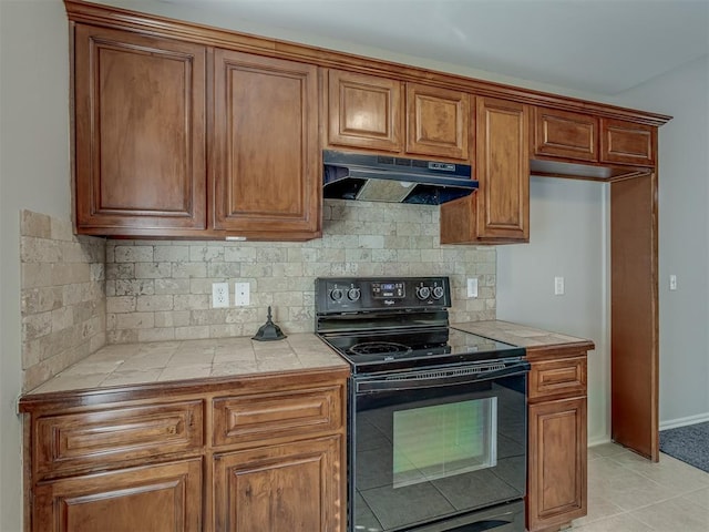 kitchen with tile countertops, backsplash, black electric range oven, and light tile patterned floors