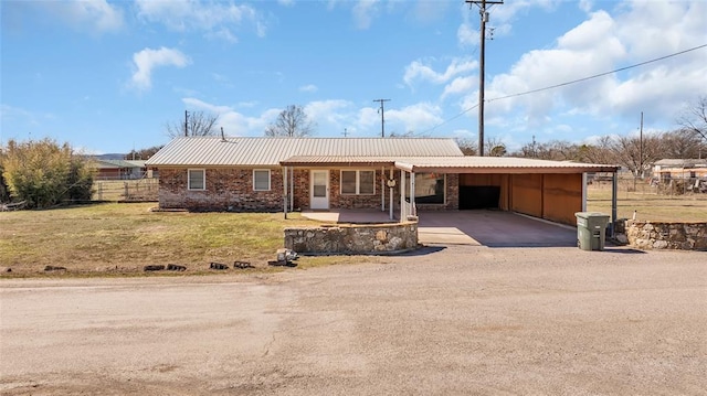 ranch-style home featuring metal roof, brick siding, dirt driveway, a carport, and a front lawn