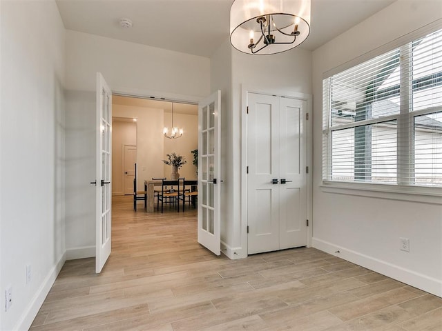 entrance foyer with baseboards, french doors, light wood finished floors, and a notable chandelier