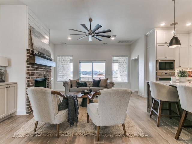 living area featuring a fireplace, light wood finished floors, recessed lighting, visible vents, and baseboards