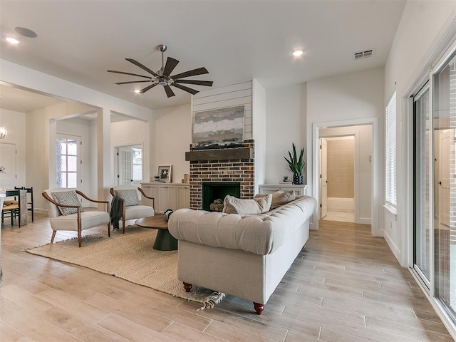 living room with light wood-style flooring, a fireplace, visible vents, and ceiling fan