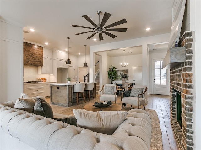 living room featuring light wood-type flooring, a brick fireplace, recessed lighting, and stairs