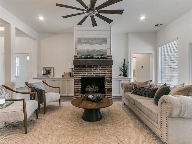 living room with light wood-style flooring, a brick fireplace, visible vents, and recessed lighting