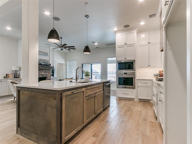 kitchen with decorative light fixtures, appliances with stainless steel finishes, a kitchen island with sink, white cabinetry, and a sink