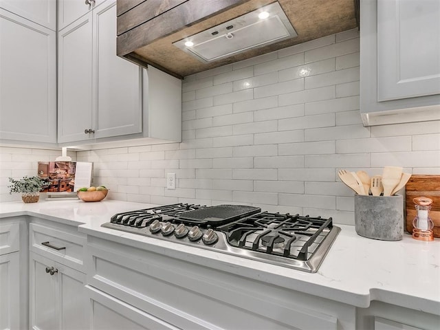 kitchen with premium range hood, stainless steel gas stovetop, white cabinetry, and tasteful backsplash