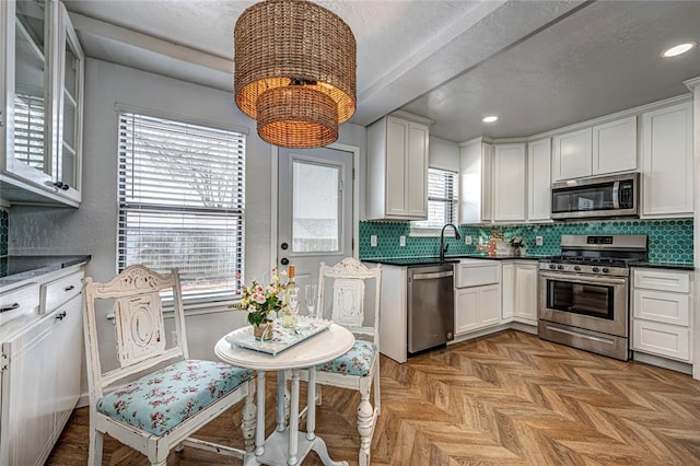 kitchen featuring tasteful backsplash, dark countertops, appliances with stainless steel finishes, white cabinets, and a sink