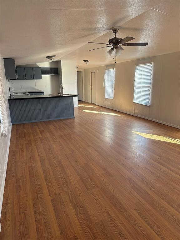 unfurnished living room with a textured ceiling, ceiling fan, a sink, wood finished floors, and baseboards