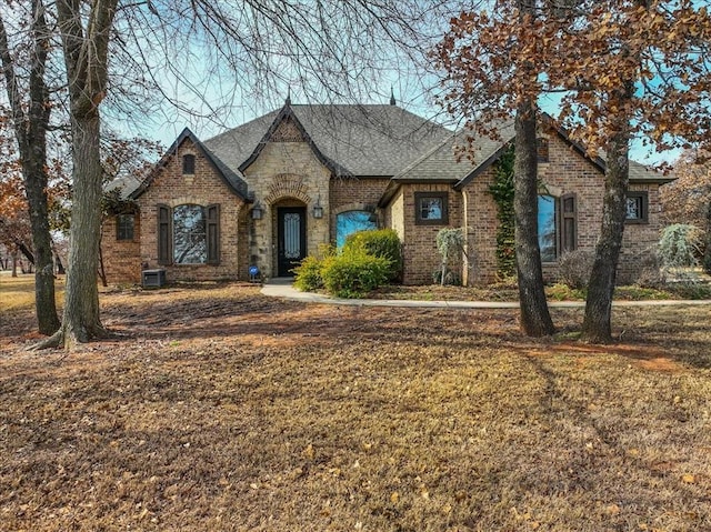 view of front of property featuring a shingled roof, a front lawn, central AC, and brick siding