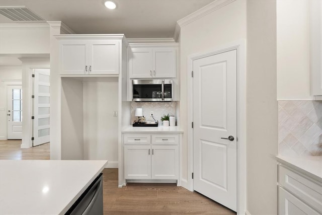 10949 Sandstone Ridge Way, Guthrie, OK 73044 - kitchen featuring stainless steel microwave, light countertops, white cabinetry, backsplash, and light wood-style floors