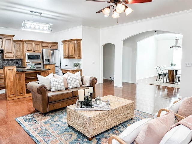 living area with baseboards, arched walkways, light wood-style flooring, crown molding, and ceiling fan with notable chandelier