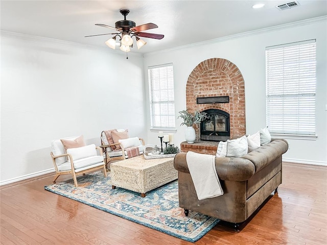 living area with baseboards, visible vents, wood finished floors, crown molding, and a brick fireplace